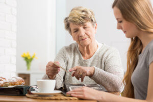 Portrait of an elderly lady having coffee with her granddaughter and showing an old photograph to her
